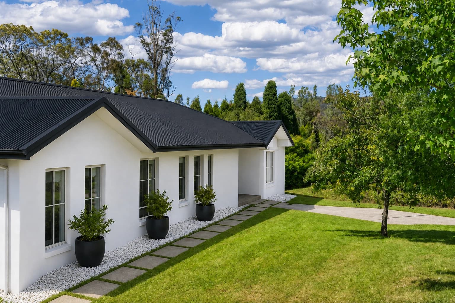 Artist's impression of the front exterior with white render, a black metal roof, an open recessed entry, a grass-jointed stone path beside the driveway, and black planters in white gravel