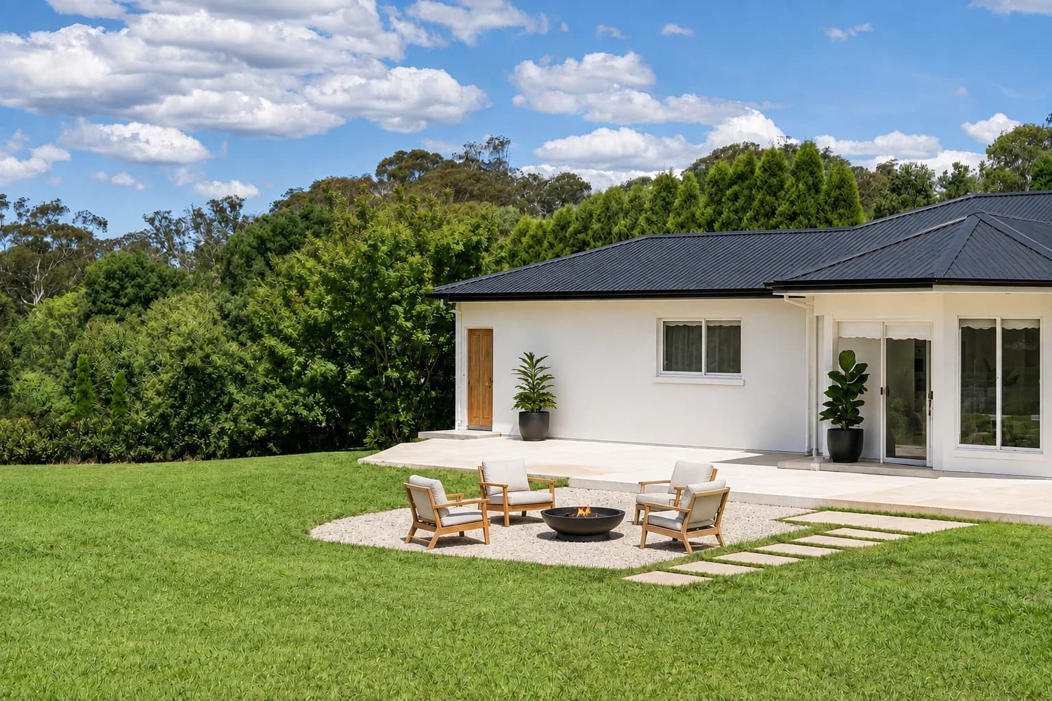 Artist's impression of the rear exterior with white render, a black metal roof, cleared low planting, black planters and a fire-pit seating area